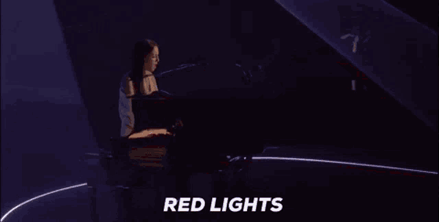 a woman is playing a piano in a dark room and the words red lights are visible