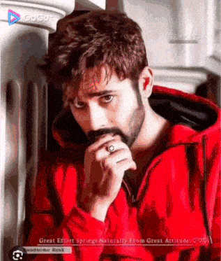 a man with a beard wearing a red hoodie and a ring on his finger .