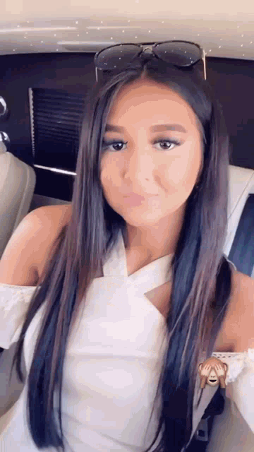 a woman wearing sunglasses and a white top is taking a selfie while sitting in a car .