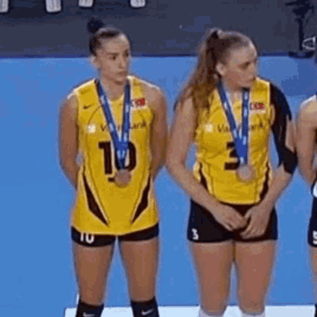 two female volleyball players wearing medals are standing next to each other on a podium .