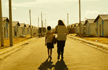 a woman and a boy are walking down a street with a row of houses in the background