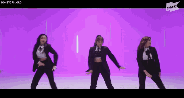 three women in suits are dancing in front of a purple background