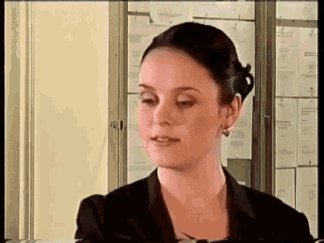 a woman in a black suit and earrings is talking to someone in a room .