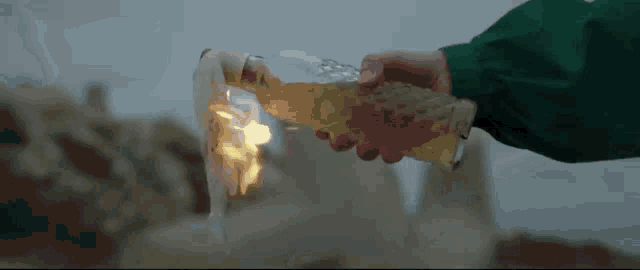a person in a green jacket is holding a bottle of beer with a flame coming out of it .