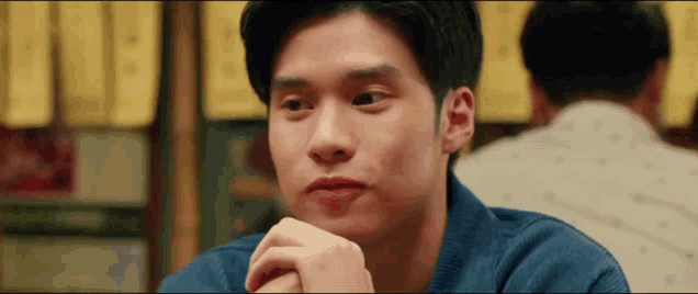 a young man is sitting at a table with his hands folded and looking at the camera .