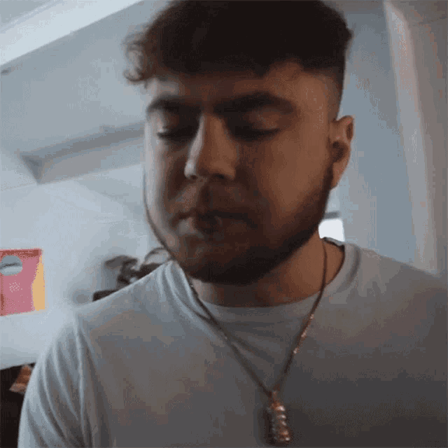 a man with a beard wearing a white shirt and a gold chain