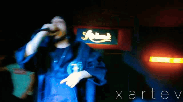 a man singing into a microphone in front of a sign that says xarev