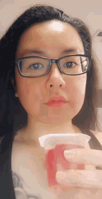 a woman wearing glasses is holding a cup of red liquid