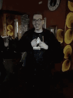 a man in a black shirt with a triangle on it holds a glass of beer