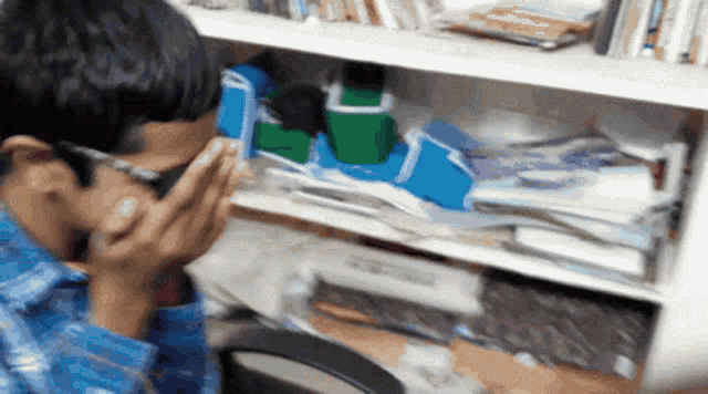 a man in a blue plaid shirt is sitting in front of a bookshelf