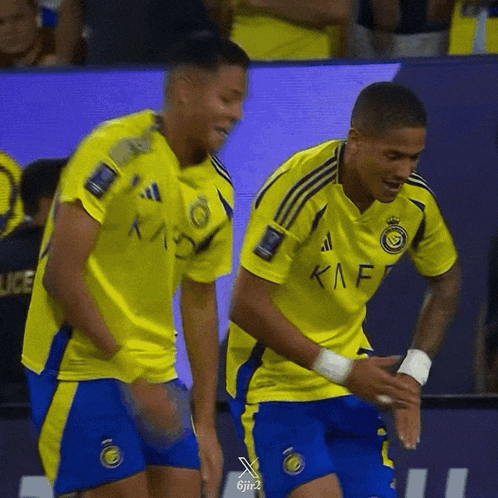two soccer players wearing yellow and blue uniforms with kaf on them