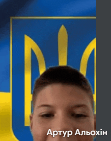 a young boy is smiling in front of a blue and yellow flag with a coat of arms