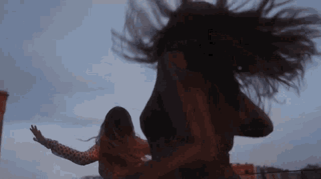 two women are dancing together on a rooftop and their hair is blowing in the wind .