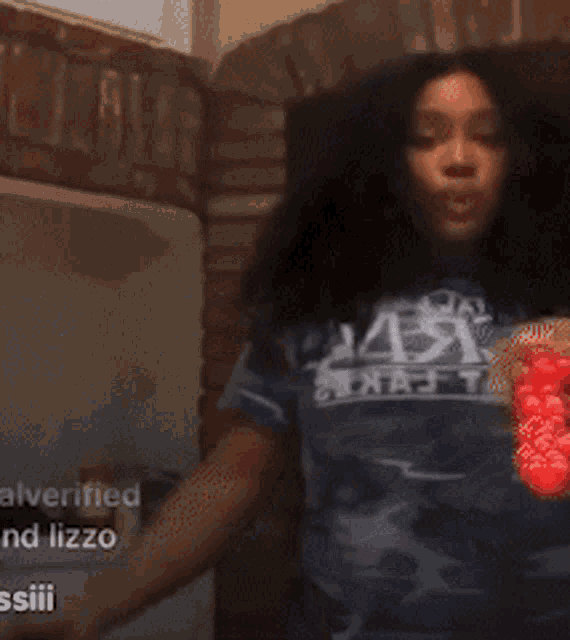 a person in a blue shirt is dancing in a room with a sign that says verified and lizzo on it .