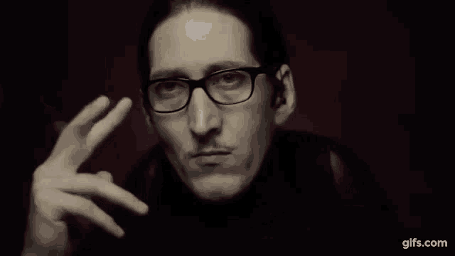 a man wearing glasses is smoking a cigarette and holding a pencil .
