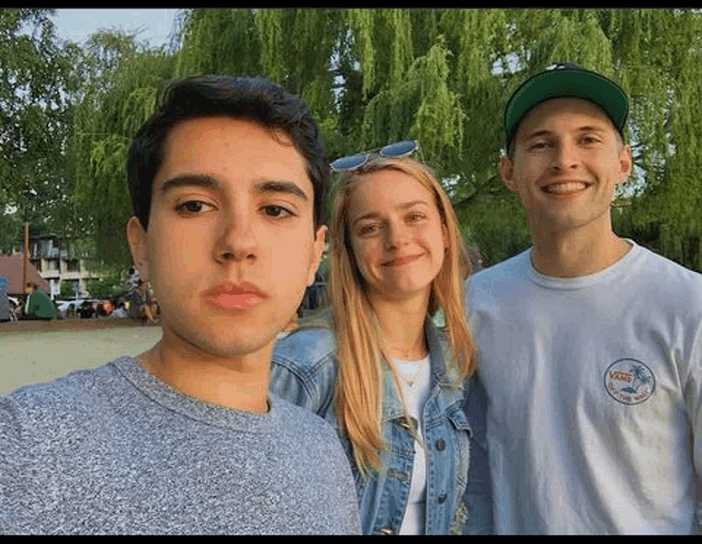 a man and two women are posing for a picture in front of a willow tree .