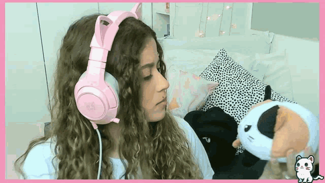 a girl wearing a pair of pink headphones looks at a stuffed cat