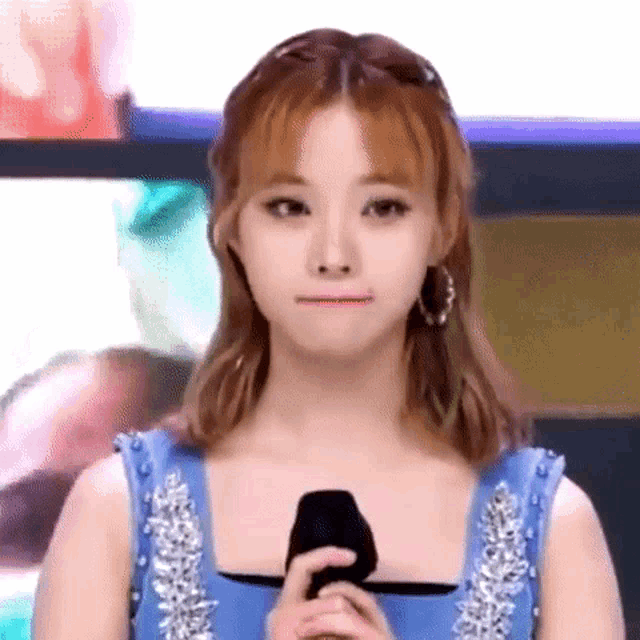 a young woman in a blue dress is holding a microphone and making a funny face .