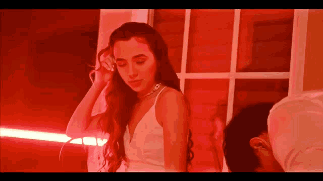 a woman in a white dress is standing in front of a window with red lights behind her