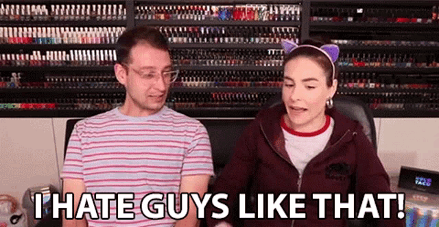 a man and a woman are sitting in front of a wall of nail polish . the woman is wearing cat ears .