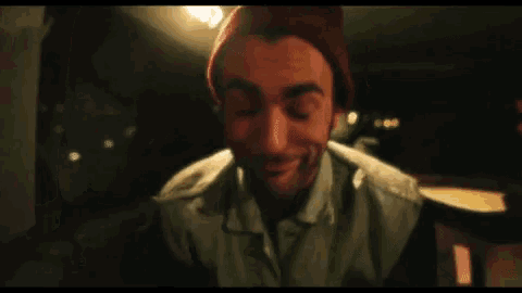 a man wearing a red hat and a white shirt is smiling while sitting in a dark room .