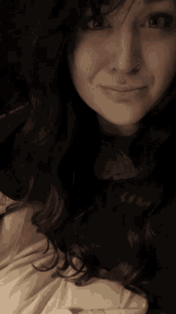 a woman with long dark hair and a nose ring smiles for the camera