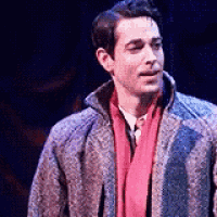a man is standing on a stage wearing a coat and scarf .