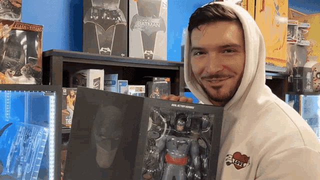 a man in a white hoodie holds a batman action figure in his hands