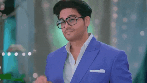 a man in a blue suit and glasses is giving a peace sign .