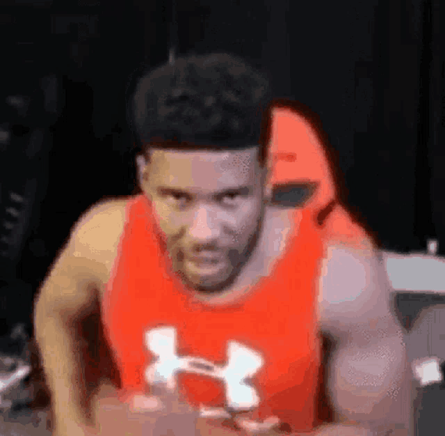 a man in a red under armour tank top is flexing his muscles in a gym .