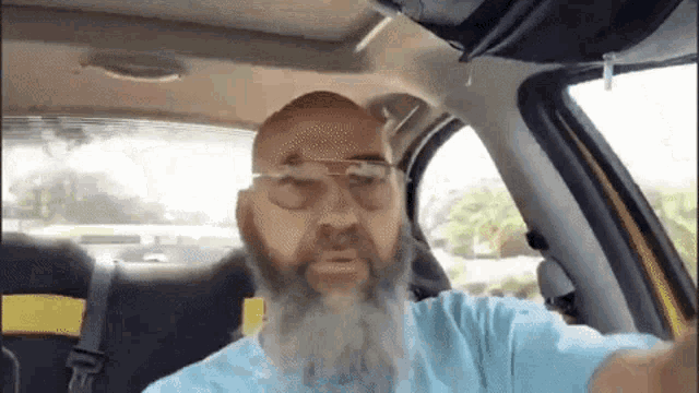 a bald man with a beard wearing glasses is sitting in the back seat of a car