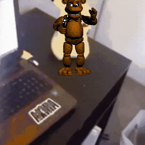 a brown teddy bear standing next to a laptop with a sticker that says mama