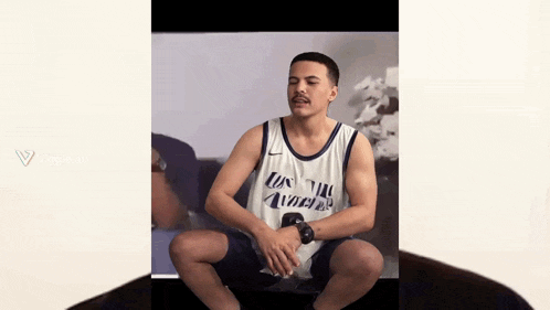 a man in a los angeles basketball jersey sits on the floor