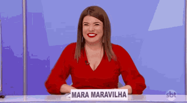 a woman in a red top is sitting at a desk with a sign that says mara maravilha