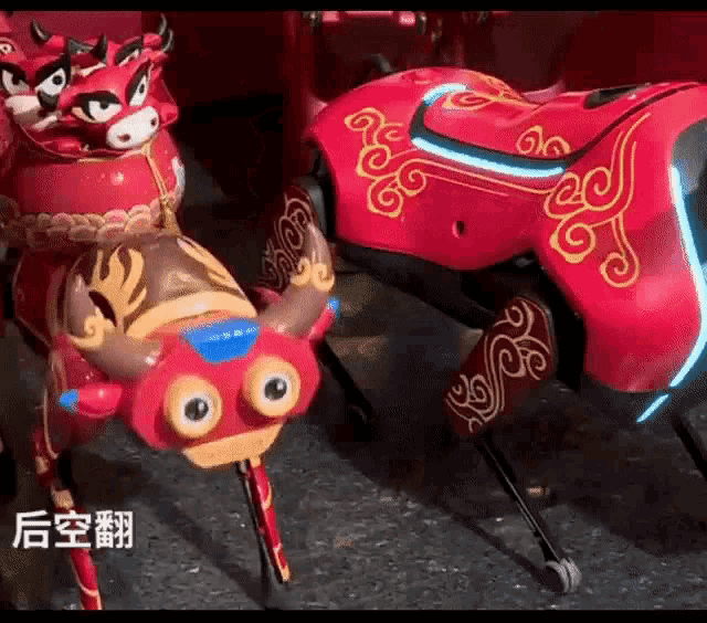 a red robot with chinese writing on it is standing next to a red bull statue .