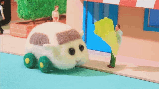 a stuffed animal with green wheels is walking down a street next to a man