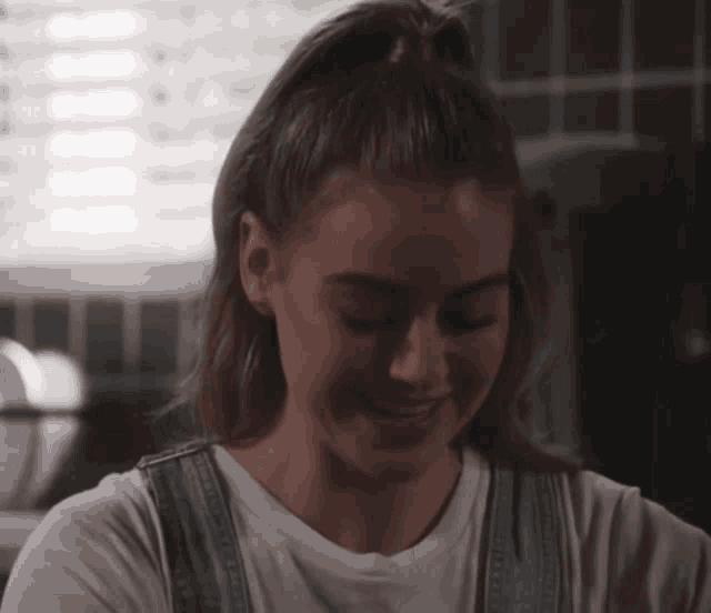 a woman wearing overalls and a white t-shirt smiles