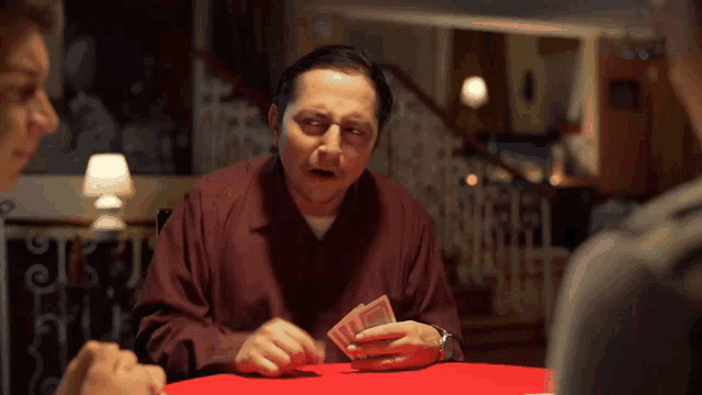 a man in a red shirt is holding a stack of money and playing cards