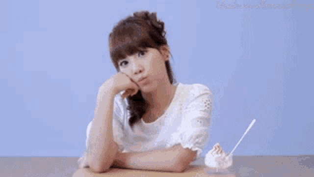 a woman in a white shirt is sitting at a table with a bowl of ice cream in front of her ..