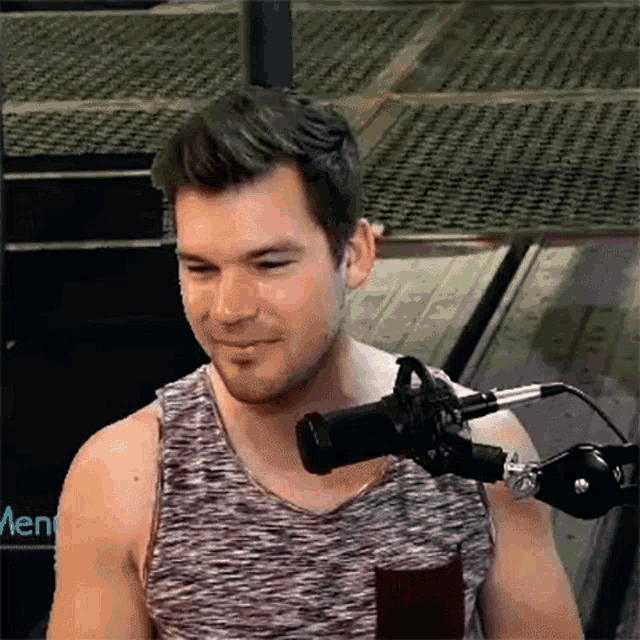 a man in a tank top is sitting in front of a microphone and smiling .