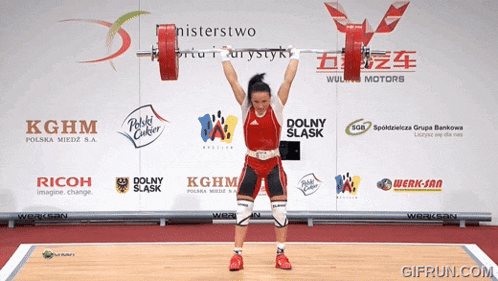 a woman lifts a barbell in front of a wall that says kghm on it