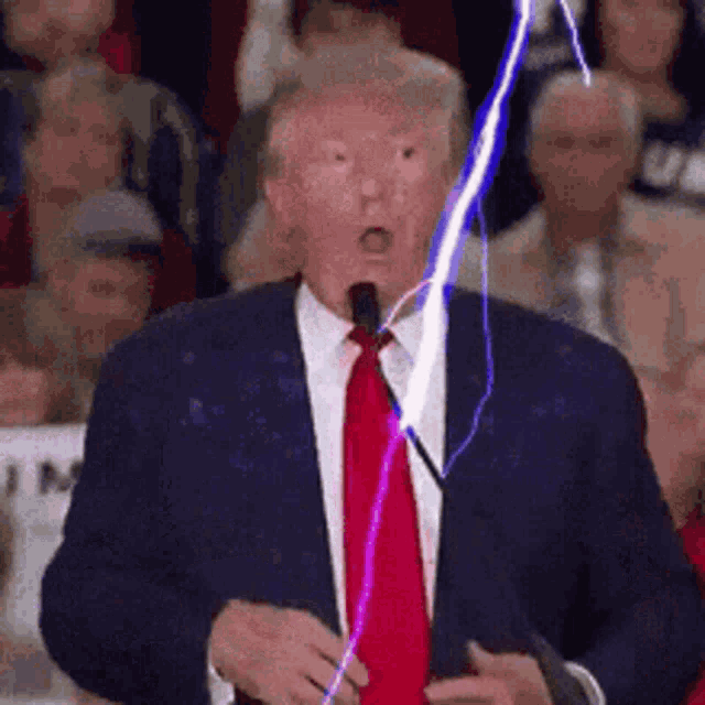 a man in a suit and tie is standing in front of a microphone and a lightning bolt is coming out of his mouth .