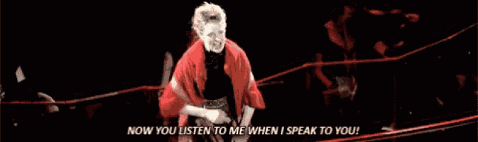 a woman in a red jacket is standing in a dark room and says `` now you listen to me when i speak to you ''