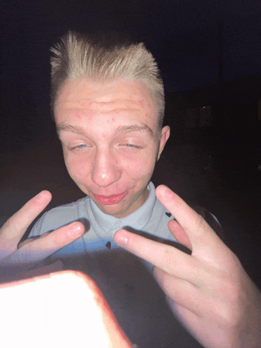 a young man with blonde hair is making a funny face with his hands