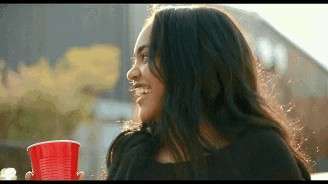a woman is holding a red cup in her hand and smiling