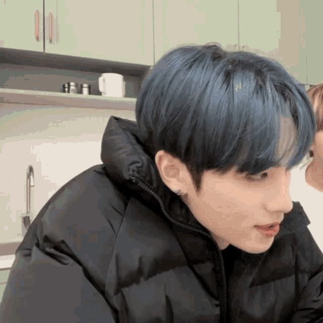a man with blue hair wearing a black jacket looks at a woman