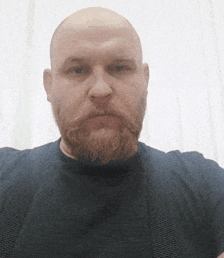 a bald man with a beard and suspenders is looking at the camera