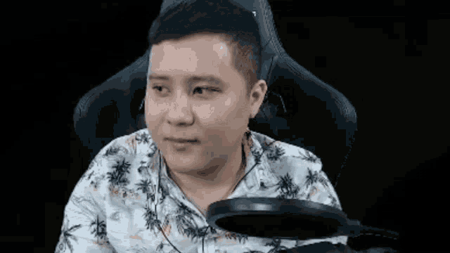 a man in a floral shirt is sitting in a chair with a microphone in front of him .