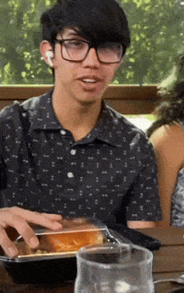 a young man wearing glasses is sitting at a table