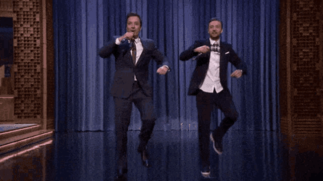 two men in suits and ties are singing into microphones on stage
